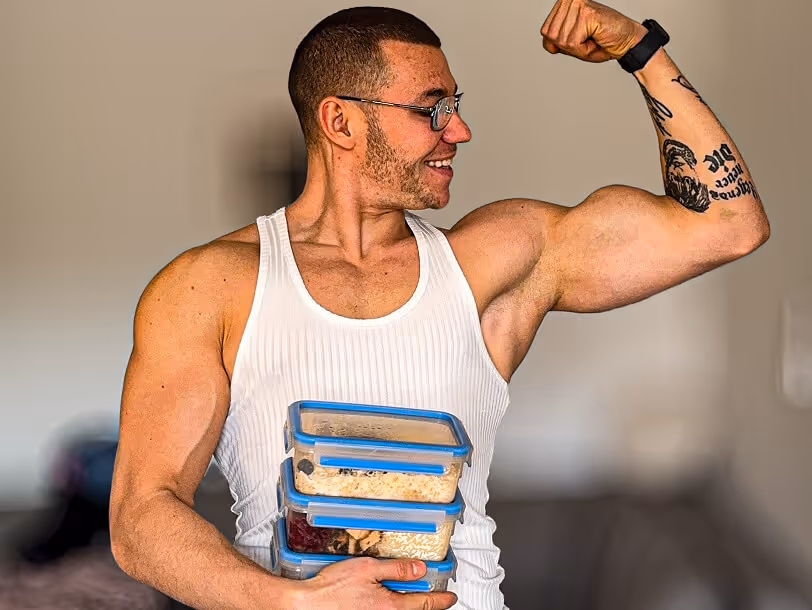 Trener personalny Robert Szałas napina swój biceps i uśmiecha się, trzymając pudełka z jedzeniem.