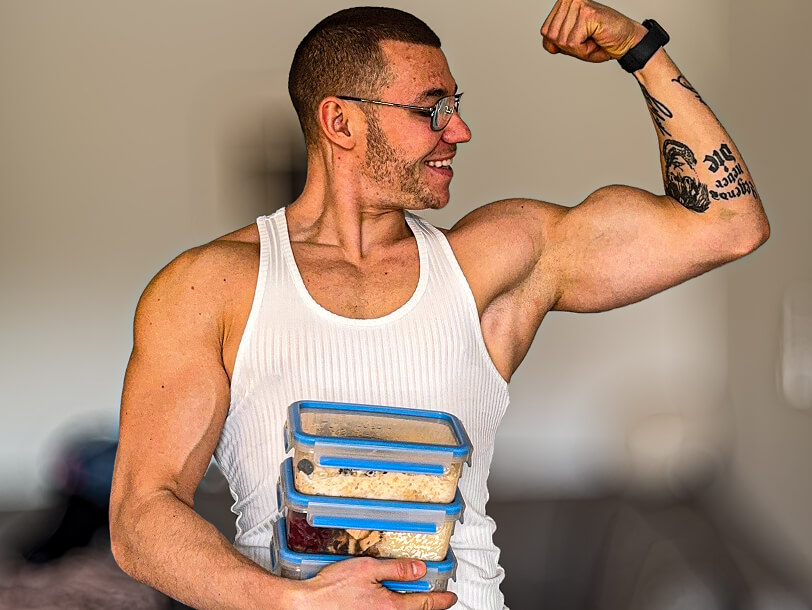 Trener personalny Robert Szałas napina swój biceps i uśmiecha się, trzymając pudełka z jedzeniem.