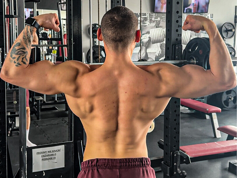 Trener personalny Robert Szałas pozuje do kamery, prezentując swoje umięśnione ramiona i plecy.