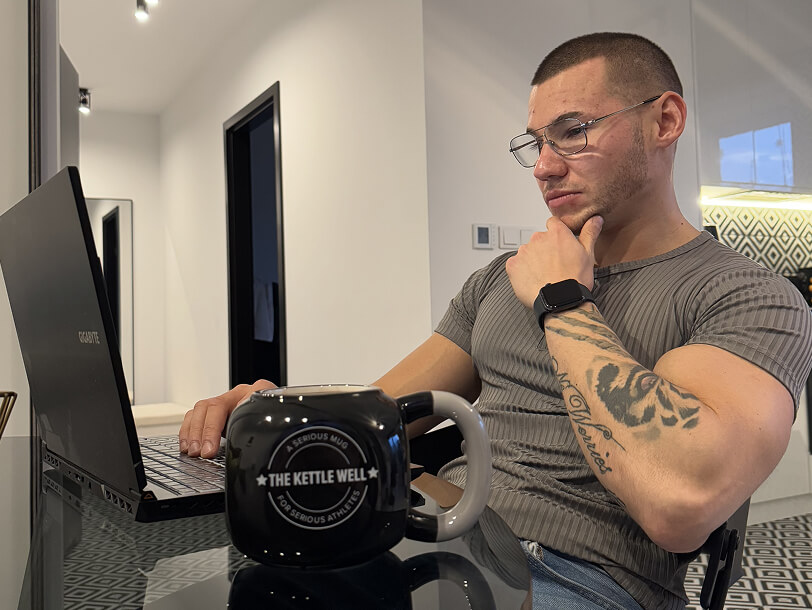 Trener personalny Robert Szałas pracuje przy laptopie nad planami treningowymi, dietetycznymi i prowadzeniem online.