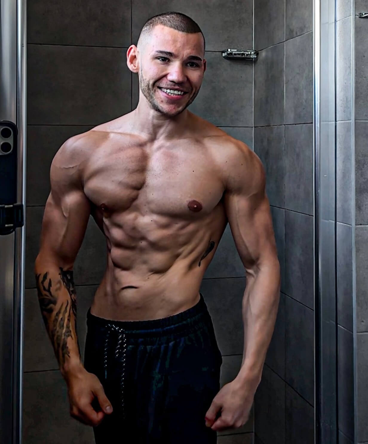 Robert Szałas, trener personalny, uśmiechnięty i umięśniony, pozuje przed lustrem w łazience, prezentując wyrzeźbioną sylwetkę.