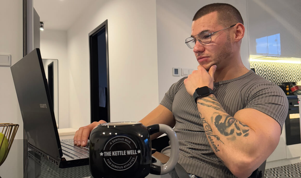 Trener personalny Robert Szałas pracuje przy laptopie nad planami treningowymi, dietetycznymi i prowadzeniem online.