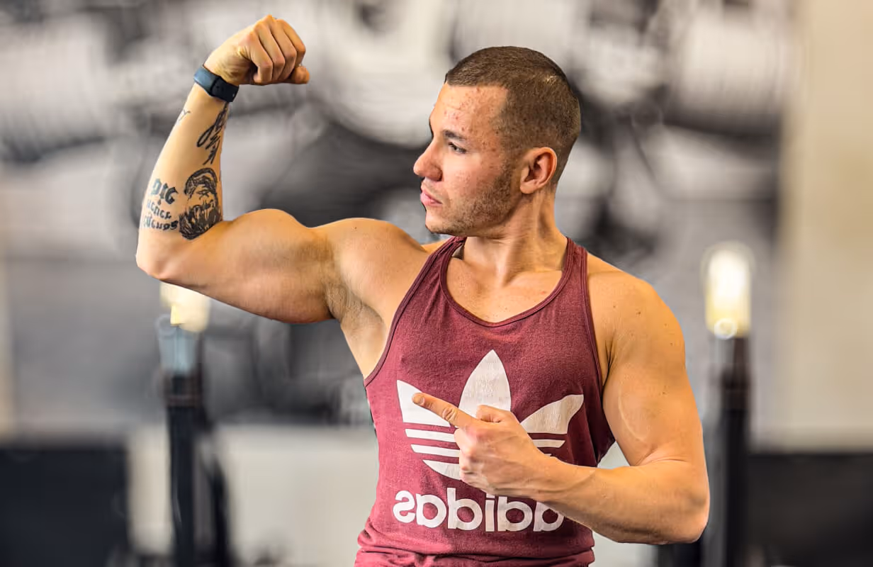 Trener personalny Robert Szałas napina biceps i wskazuje w lewo, zachęcając do przejścia na stronę z treningami personalnymi lub planami online.