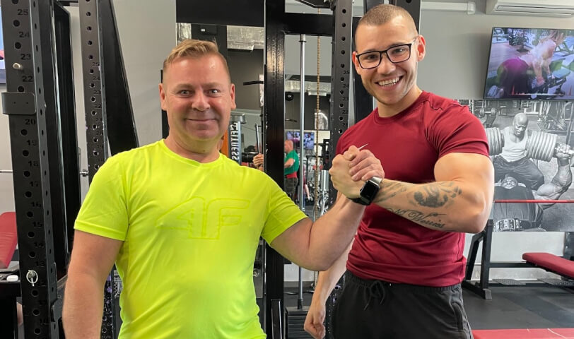 Trener personalny Robert Szałas przybija piątkę ze swoim podopiecznym, oboje są uśmiechnięci.